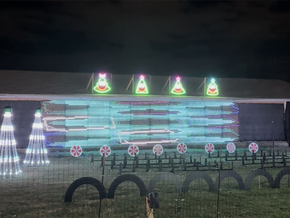 holiday light display featuring a wall with zig-zagging lights in front of two Christmas trees and rows of lollipop-shaped lights on the ground