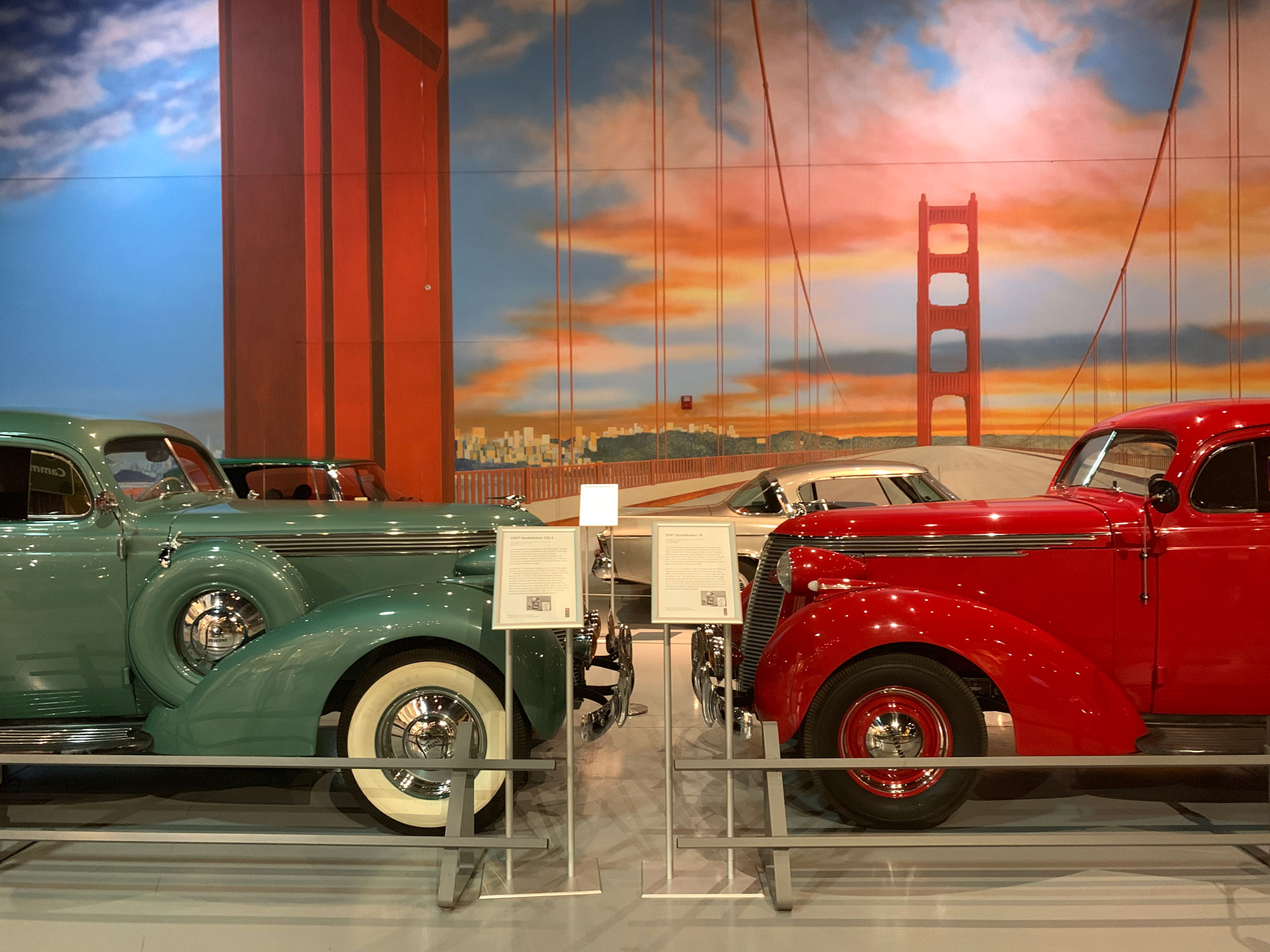 Two Studebakers posed nose-to-nose in front of a painted backdrop depciting the Golden Gate Bridge