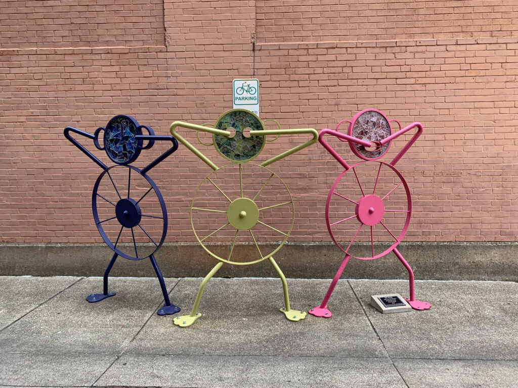 Three wire statues made with bike wheels as the base depicting see no evil, hear no evil, speak no evil