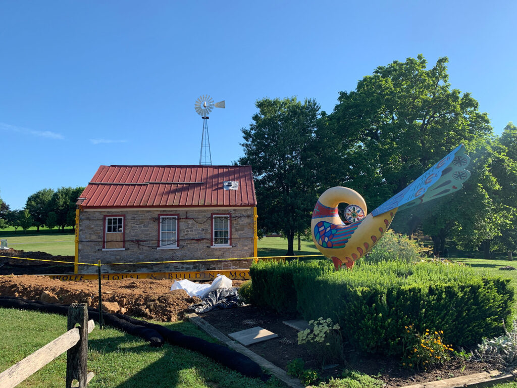 distelfink (blue and yellow folk art bird) statue in front of a one-room schoolhouse