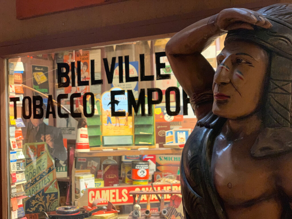 Cigar store Indian in front of a window looking into a recreated tobacco shop