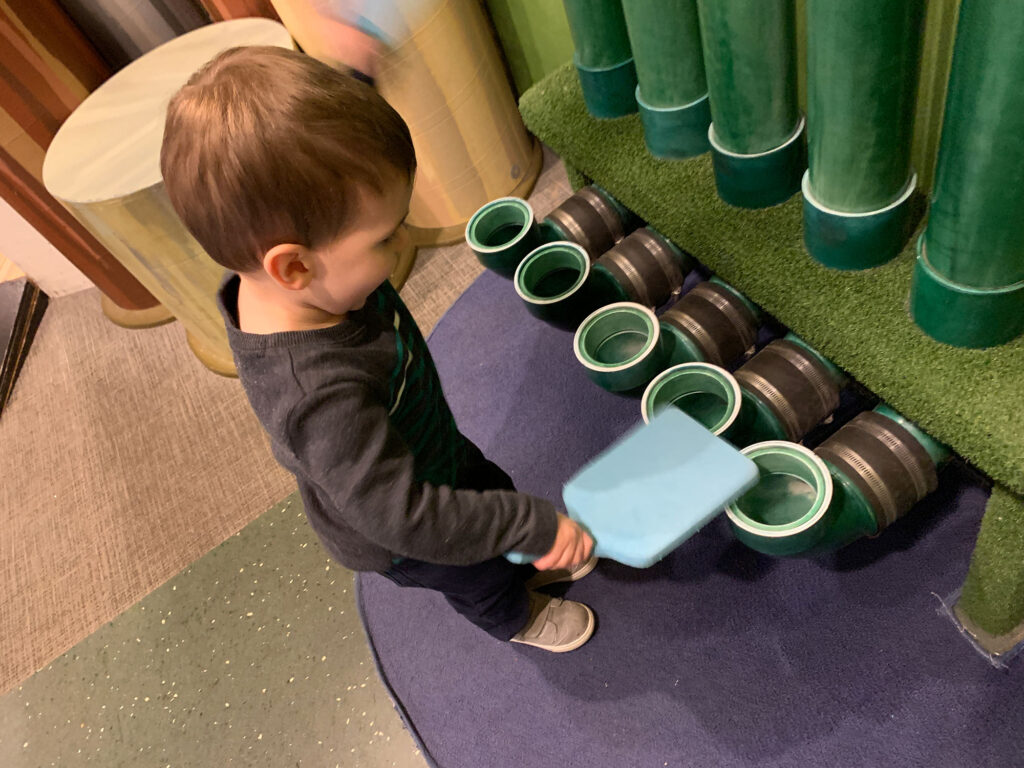 child playing with a paddle and PVC pipes to make music at the Bucks County Children's Museum