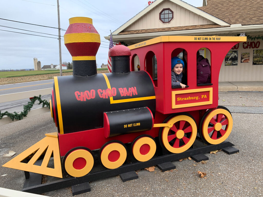 young child takes a picture inside a wooden play train at the Choo Choo Barn