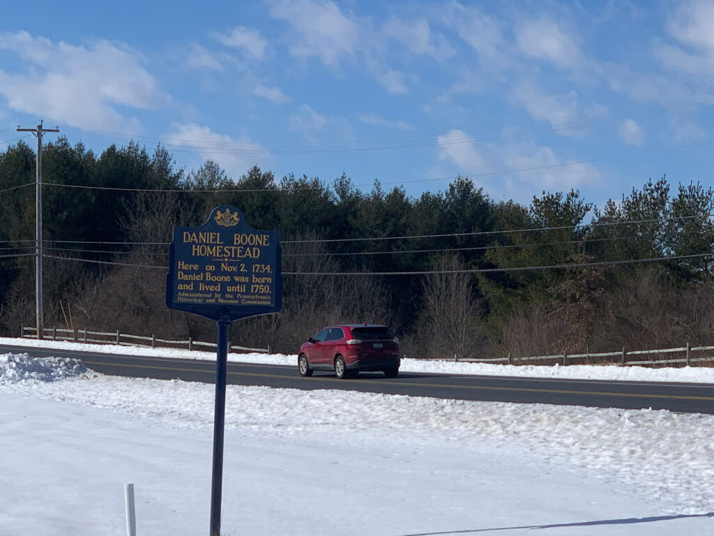 A red car passes by a PA state historical marker for the Daniel Boone Homestead in Berks County, PA