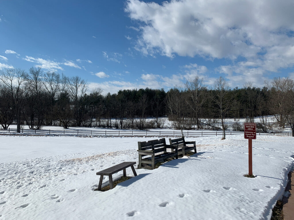 park bench in a snowy field with footprints leading to and away