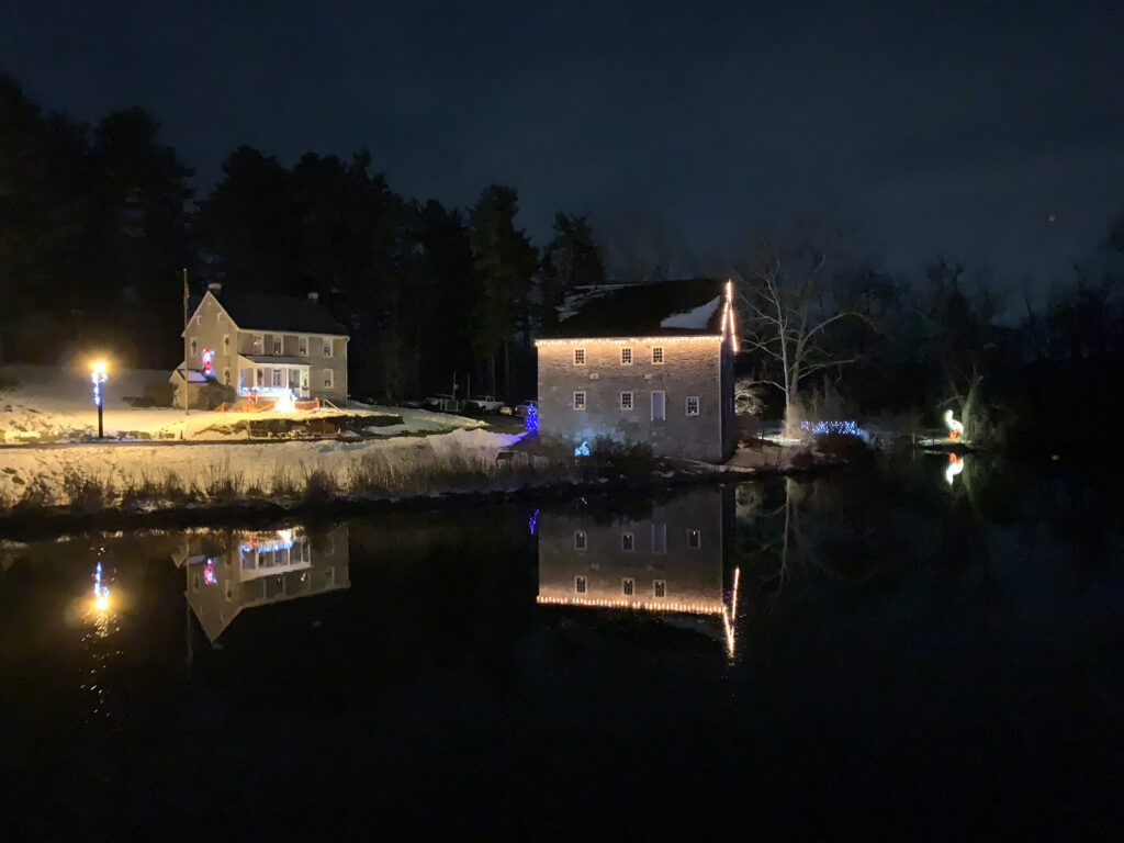 Historic stone barn illuminated by lights along the roof that refelct into the water nearby