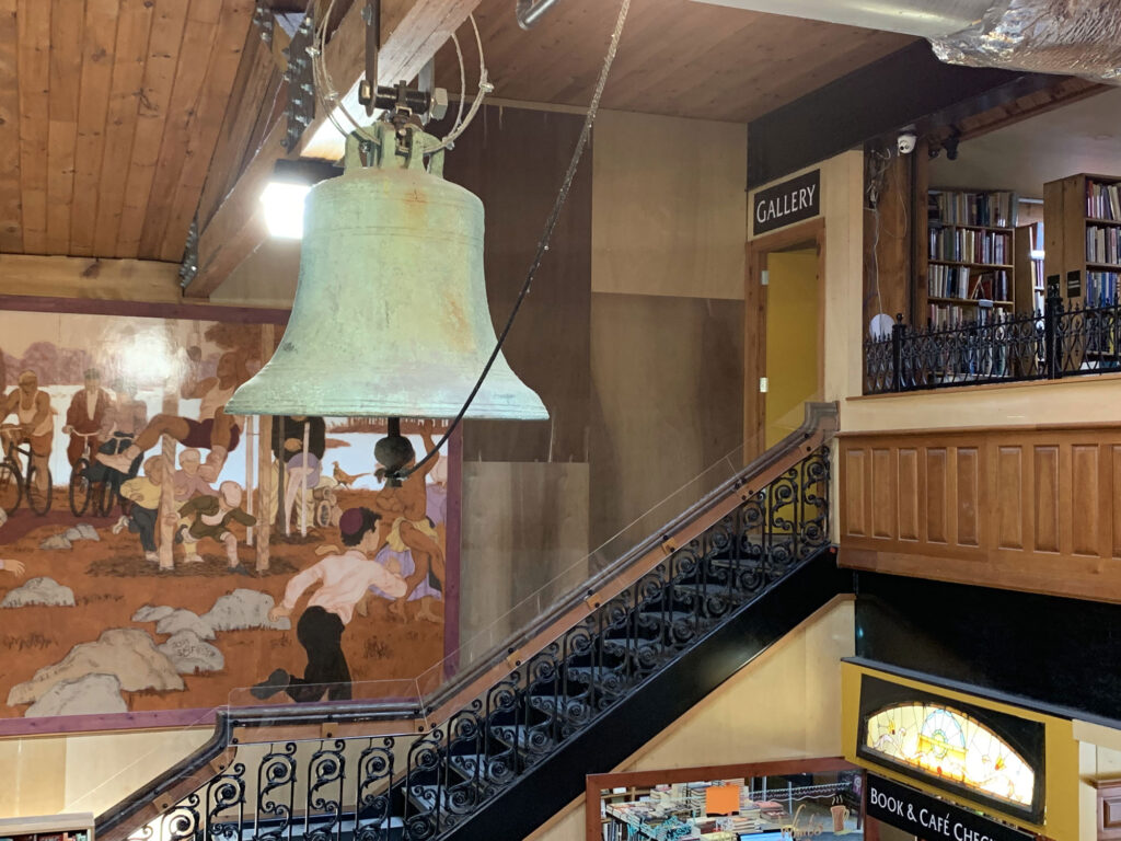 Metal bell with green petina hanging above the main hall of the Midtown Scholar Bookstore in Harrisburg, PA