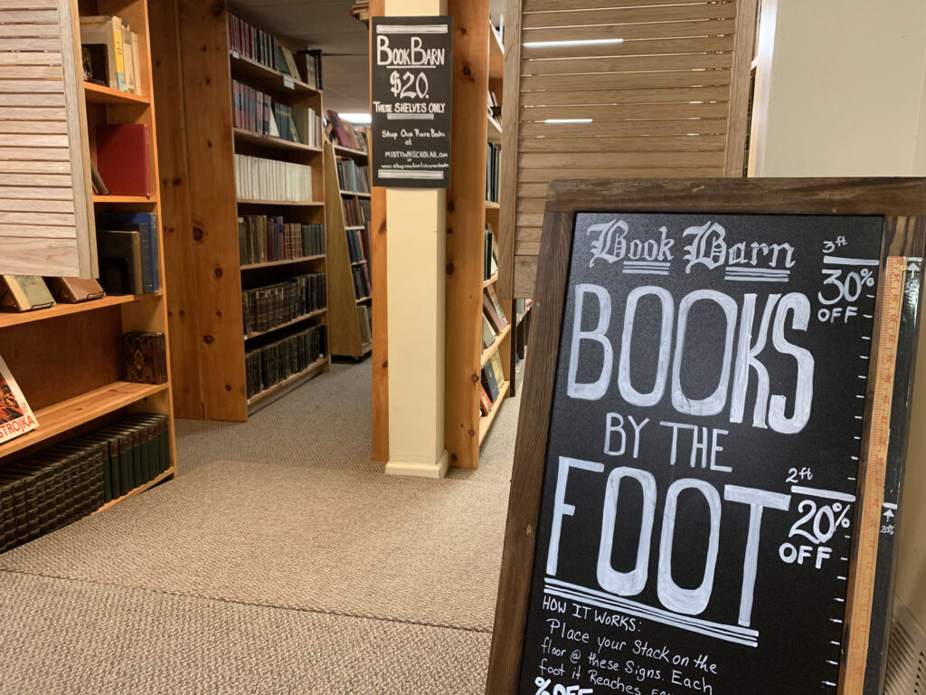 Sandwichboard sign advertising "Books by the Foot" with a ruler to mark the heigh needed to get a percentage off