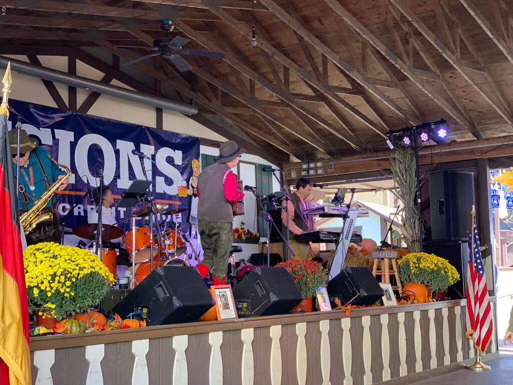 polka band with accordions and guitars plays on a stage decorated with fall mums