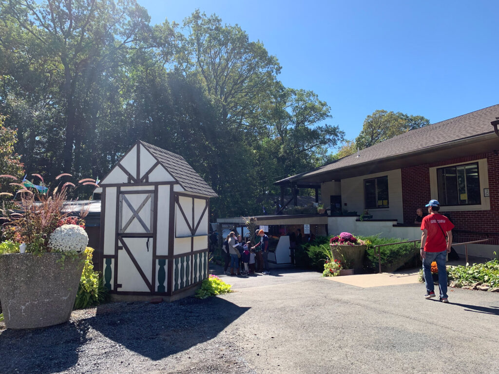 Small white Tudor-style shed on a paved pathway with a larger building in the background