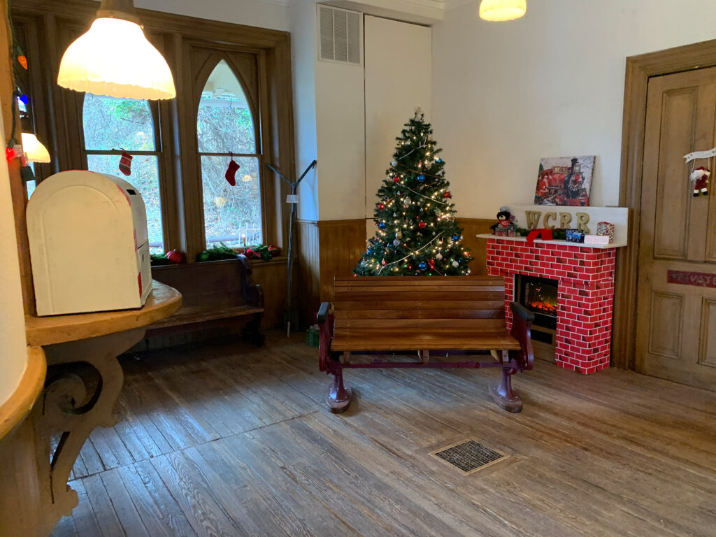 Christmas tree behind a bench on a hardwood floor inside the Glen Mills Train Station