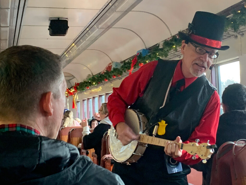 man in a top hat playing a banjo aboard a train passenger coach