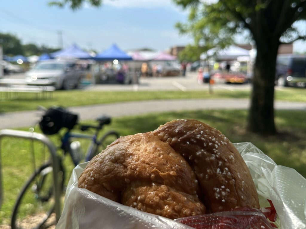 close-up of a soft pretzel with tents of a farmers market blurred in the background