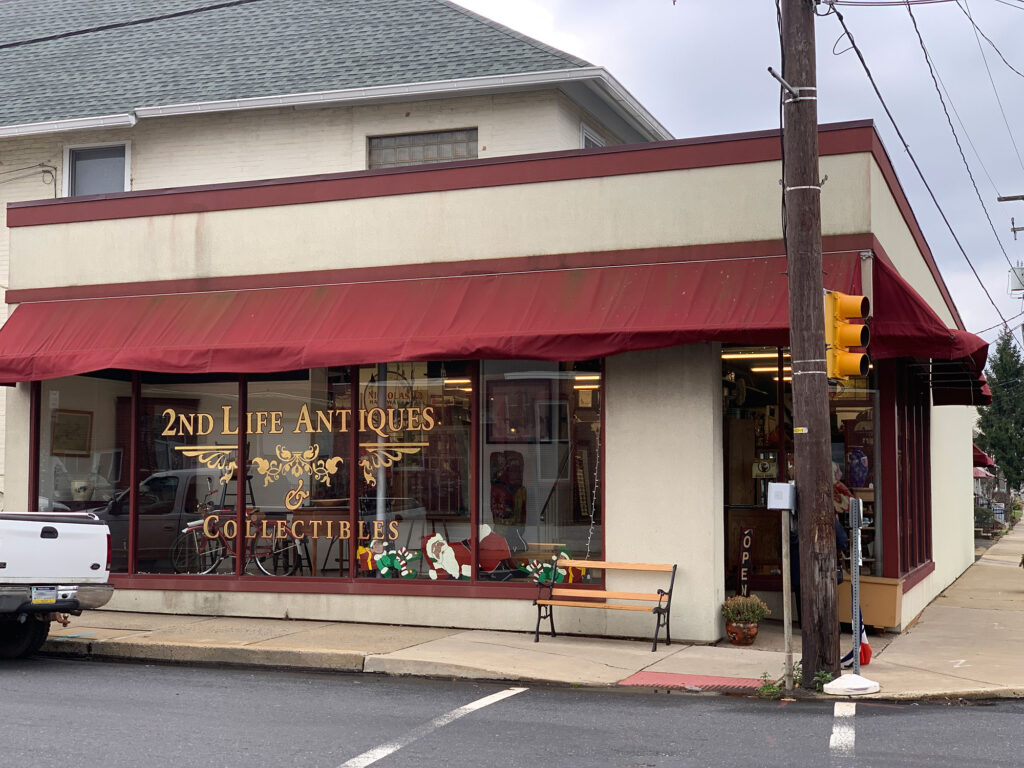 Exterior of a corner building with red awning and yellow lettering on the windows reading 2nd Life Antiques