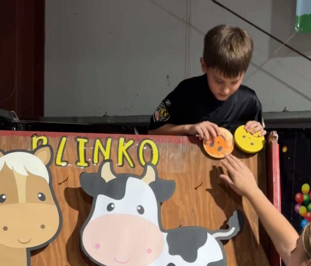 child holds a disk against wooden homemade Plinko board with a cow cutout 