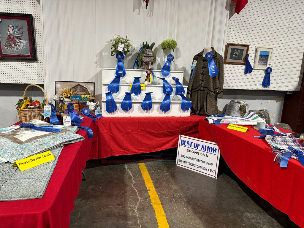 Three tables forming a U shape filled with items awarded with blue ribbons for best of show at the Bedford County Fair