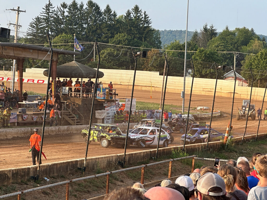 Cars scattered along a straight on a dirt track during a demolition derby