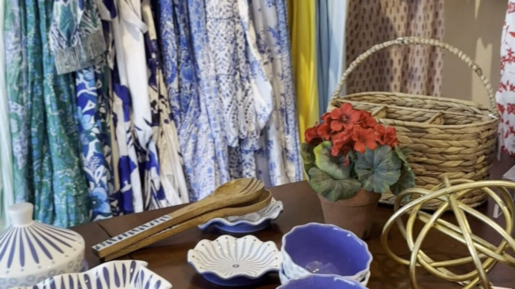 home decor items sit on a wooden table in front of a rack of clothes at Chosen Selections in Wayne, PA