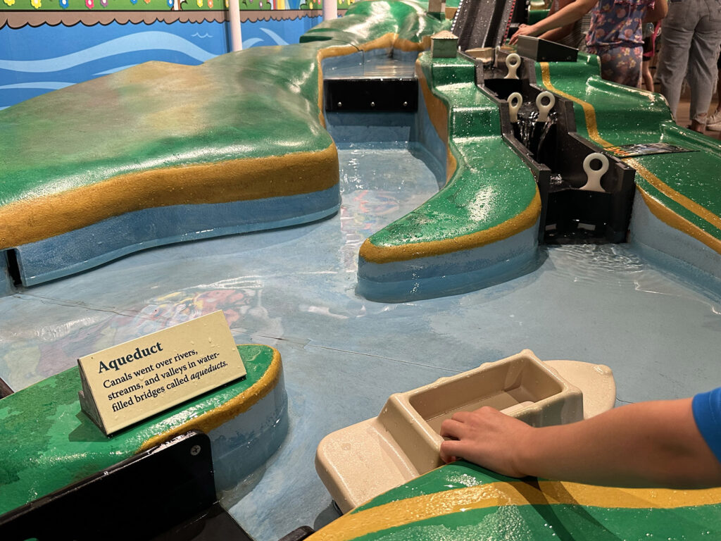 child pushing a model boat through a model canal