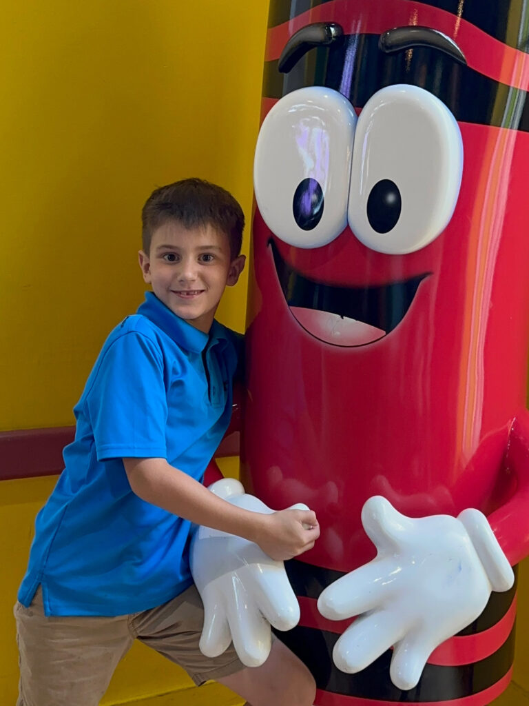 child hugging a life-size red crayon cartoon character