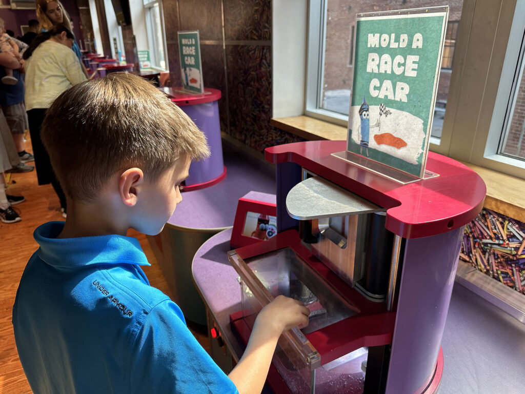 child standing by a machine that is molding crayon wax into a race car shape