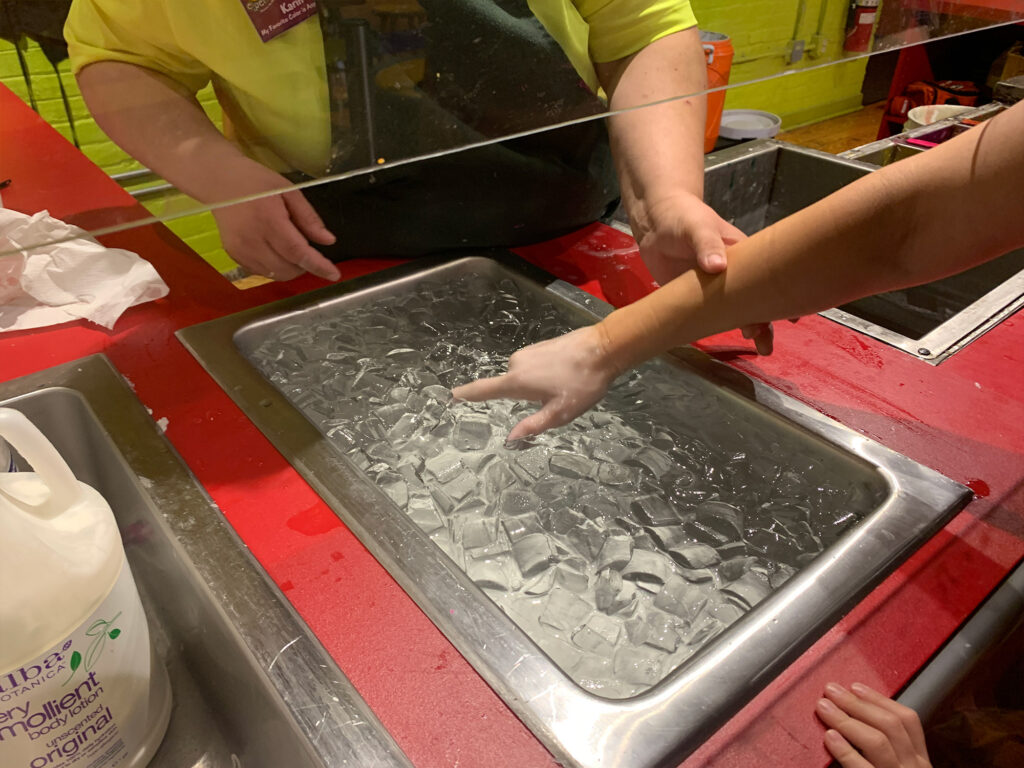 woman with wax on her hand having her hand dipped in ice water after