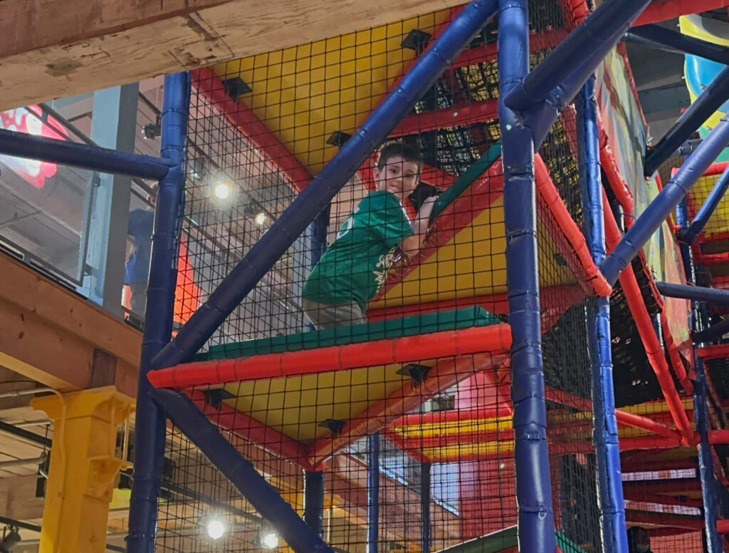 child at the top of a large indoor play structure at the Crayola Experience