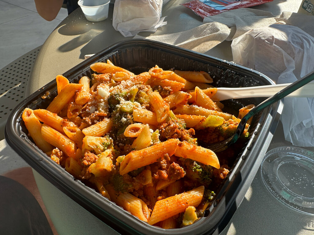 square plastic container with penne pasta covered in meat sauce