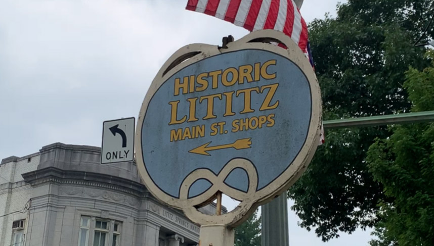 round sign reading "Historic Lititz Shops" with an arrow pointing left and a pretzel drawn on the bottom