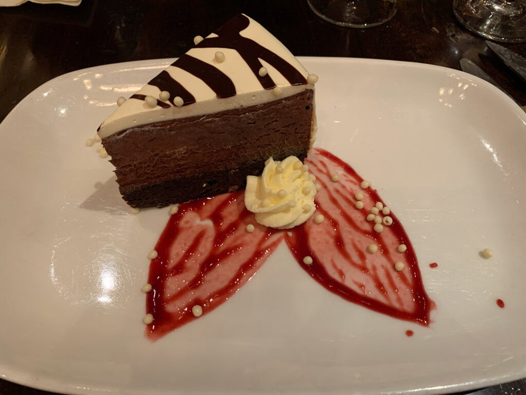 plate with a slice of chocolate cake with strawberry drizzled in the shape of a flower petal