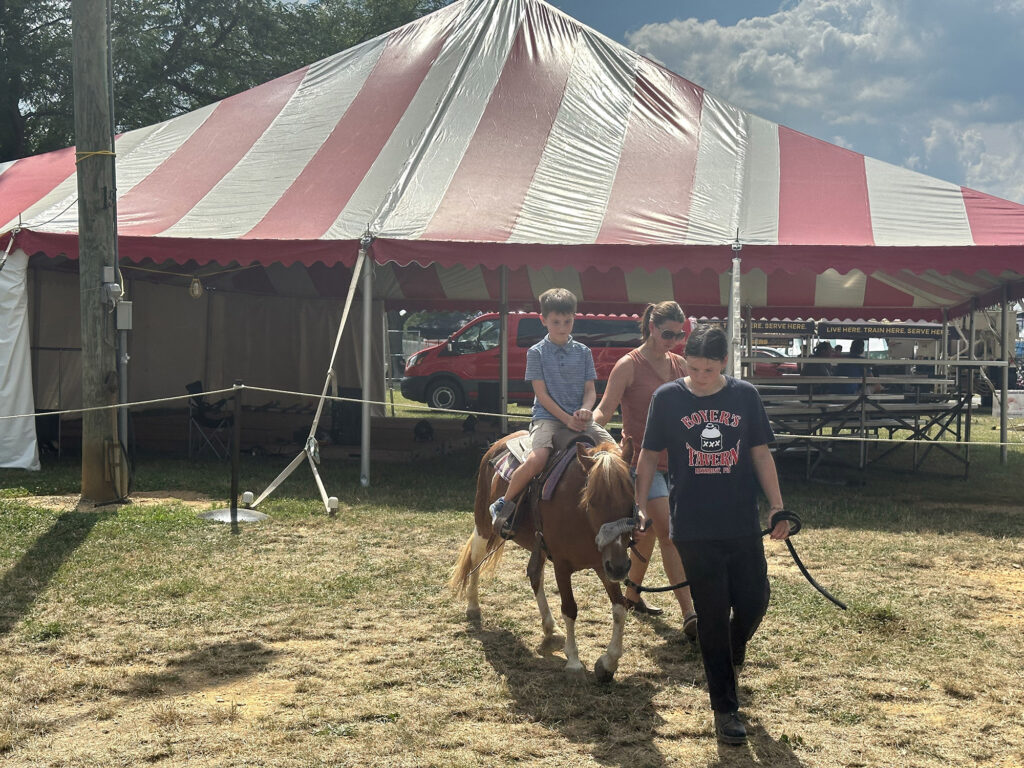 young boy riding a pony that is being led around a ring by two women