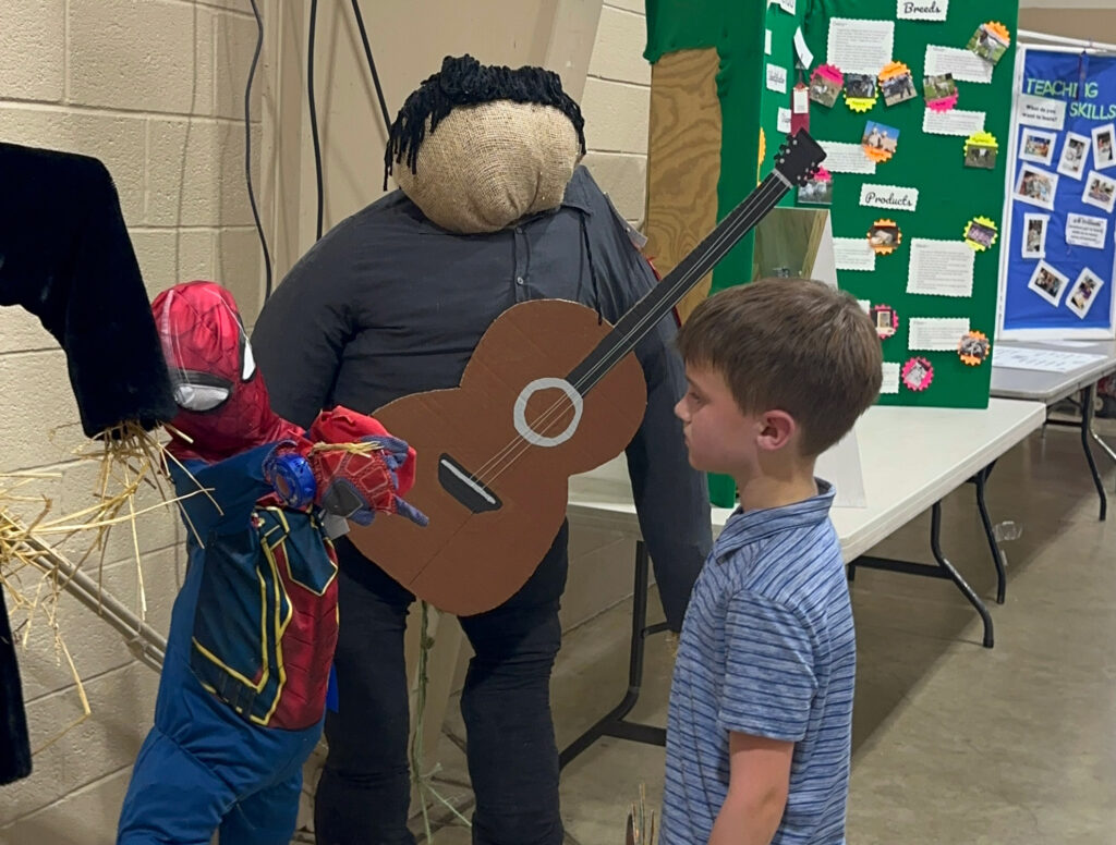 young boy standing in front of a Spider-Man scarecrow