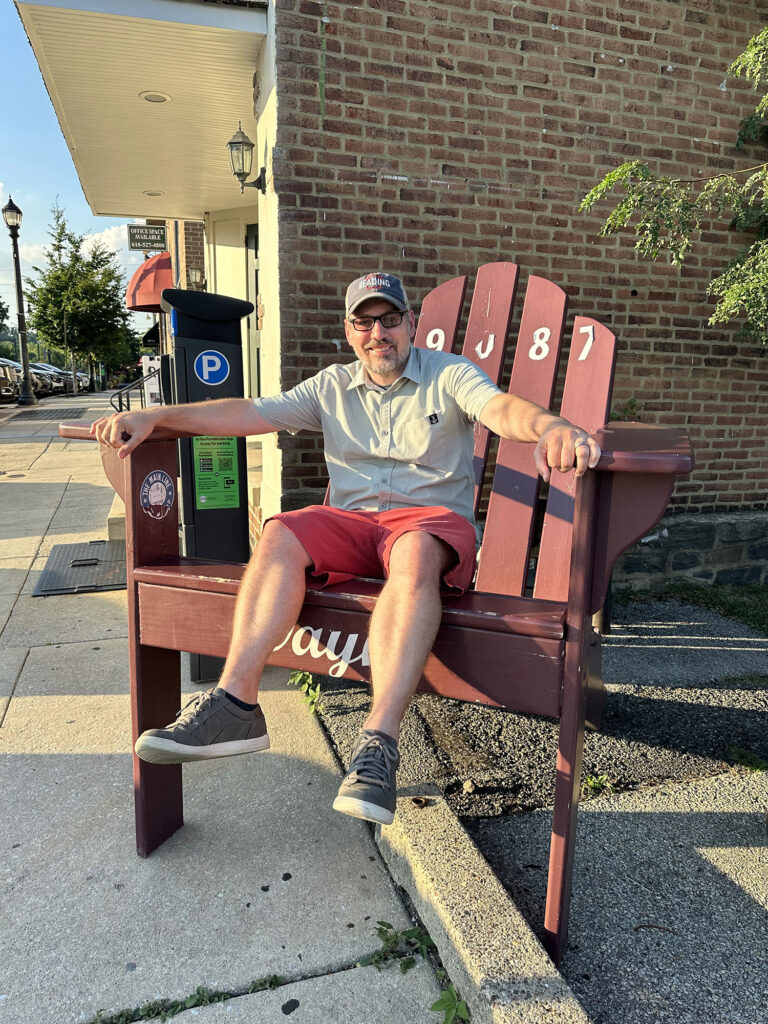 man sitting on a giant wooden chair along the street in Wayne, PA