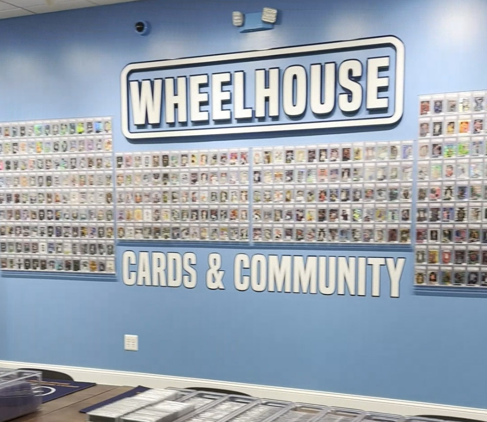 Wall graphic that reads "Wheelhouse Cards & Community" with the words surrounded by trading cards in protective cases