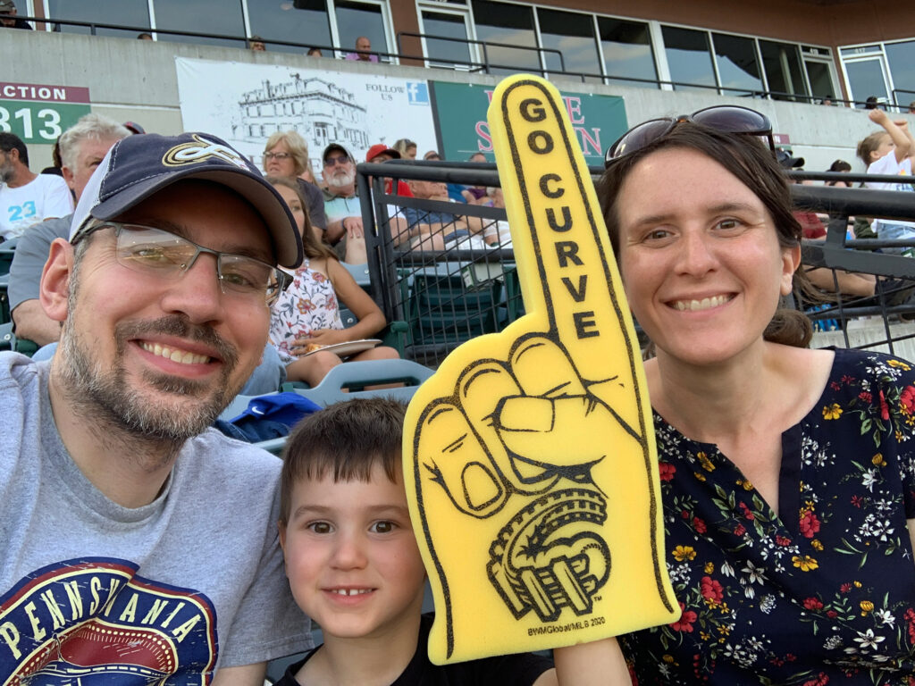 father and mother on either side of a young boy who is holding a yellow foam finger that reads "Go Curve"