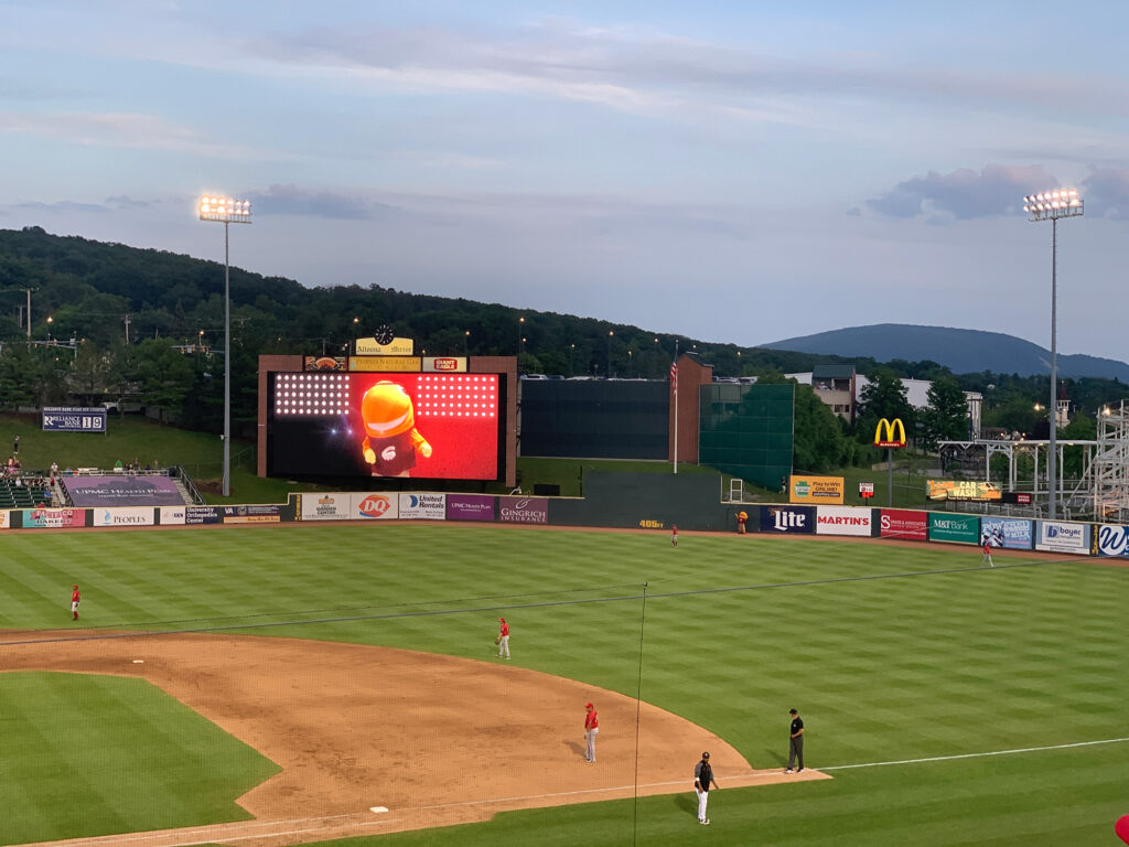 Fish mascot stepping out of the center field wall while his video plays on the big screen