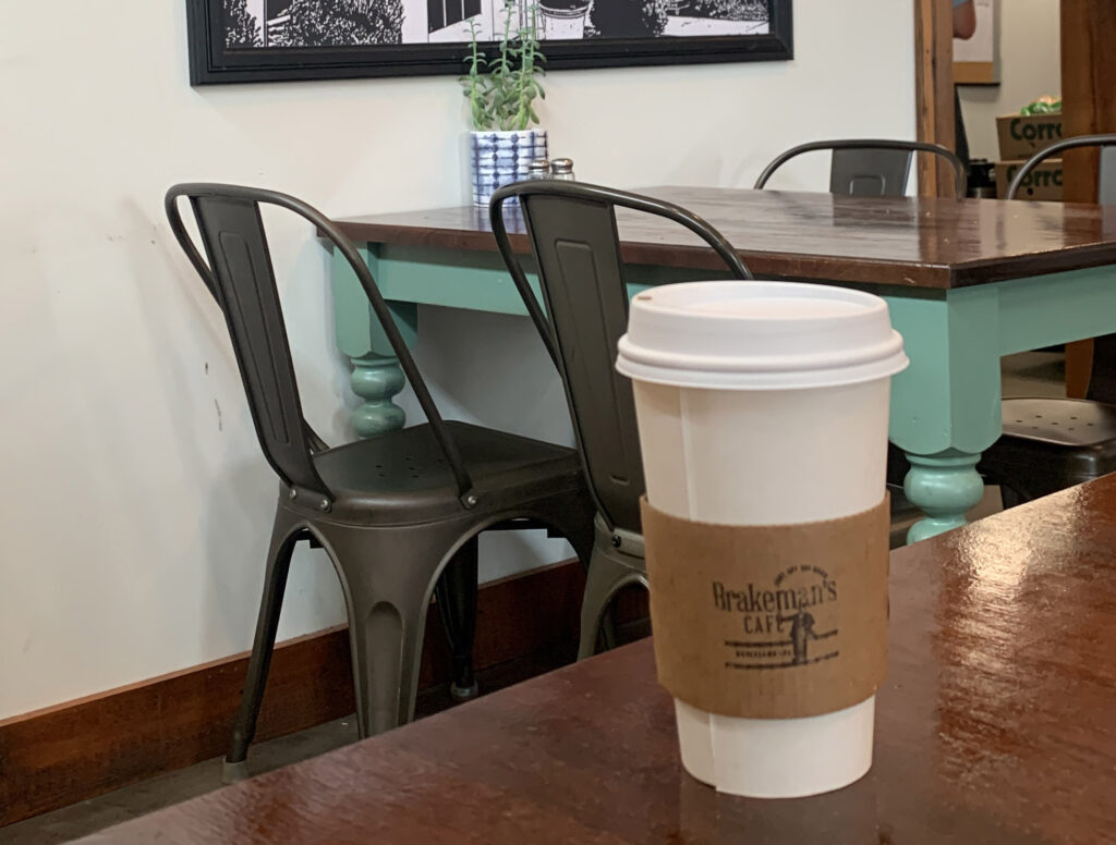 White disposable coffee cup wrapped with a brown carboard reading "Brakeman's Cafe"