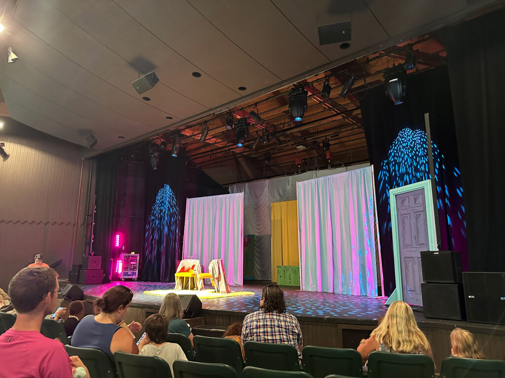 stage with two large purple curtains and two empty chairs in the spotlight