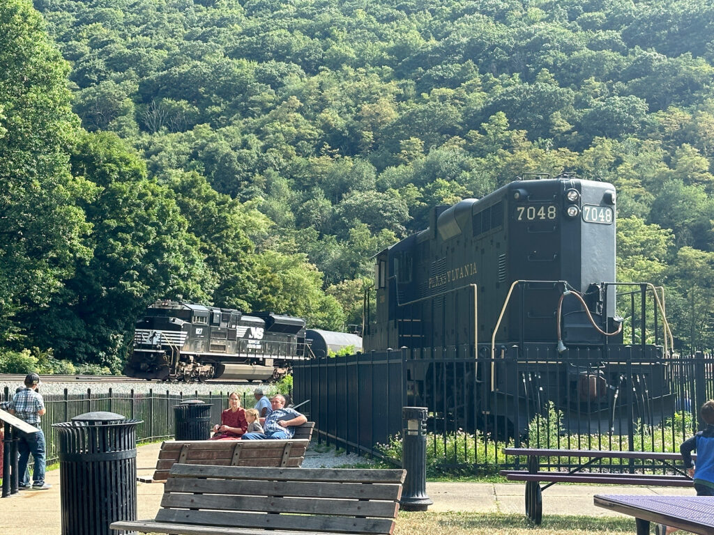 Norfolk Southern engine passing behind a historic Pennsylvania Railroad diesel engine on display at the Horseshoe Curve