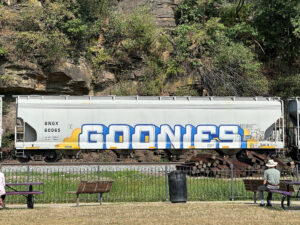 gray tanker car with the word "Goonies" in white graffiti with blue highlgihts