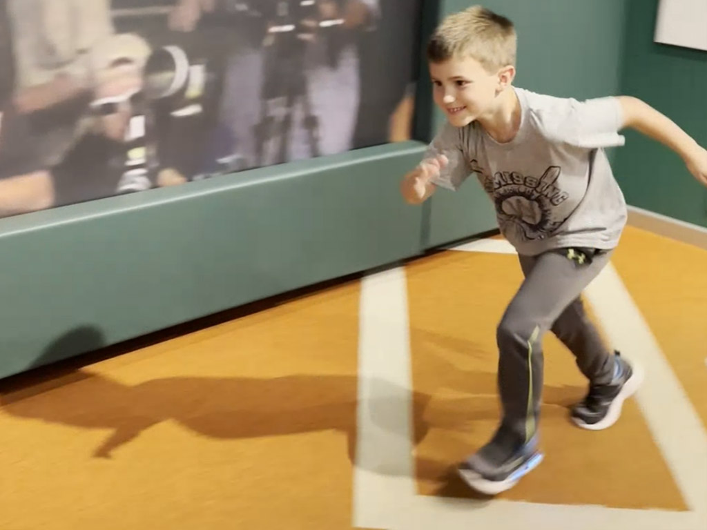 a young boy runs on a replica Little League baseball basepath