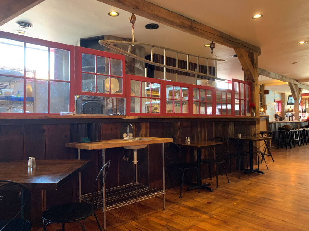 Long counter with red window boxes behind tables of two at Other Farm Brewing