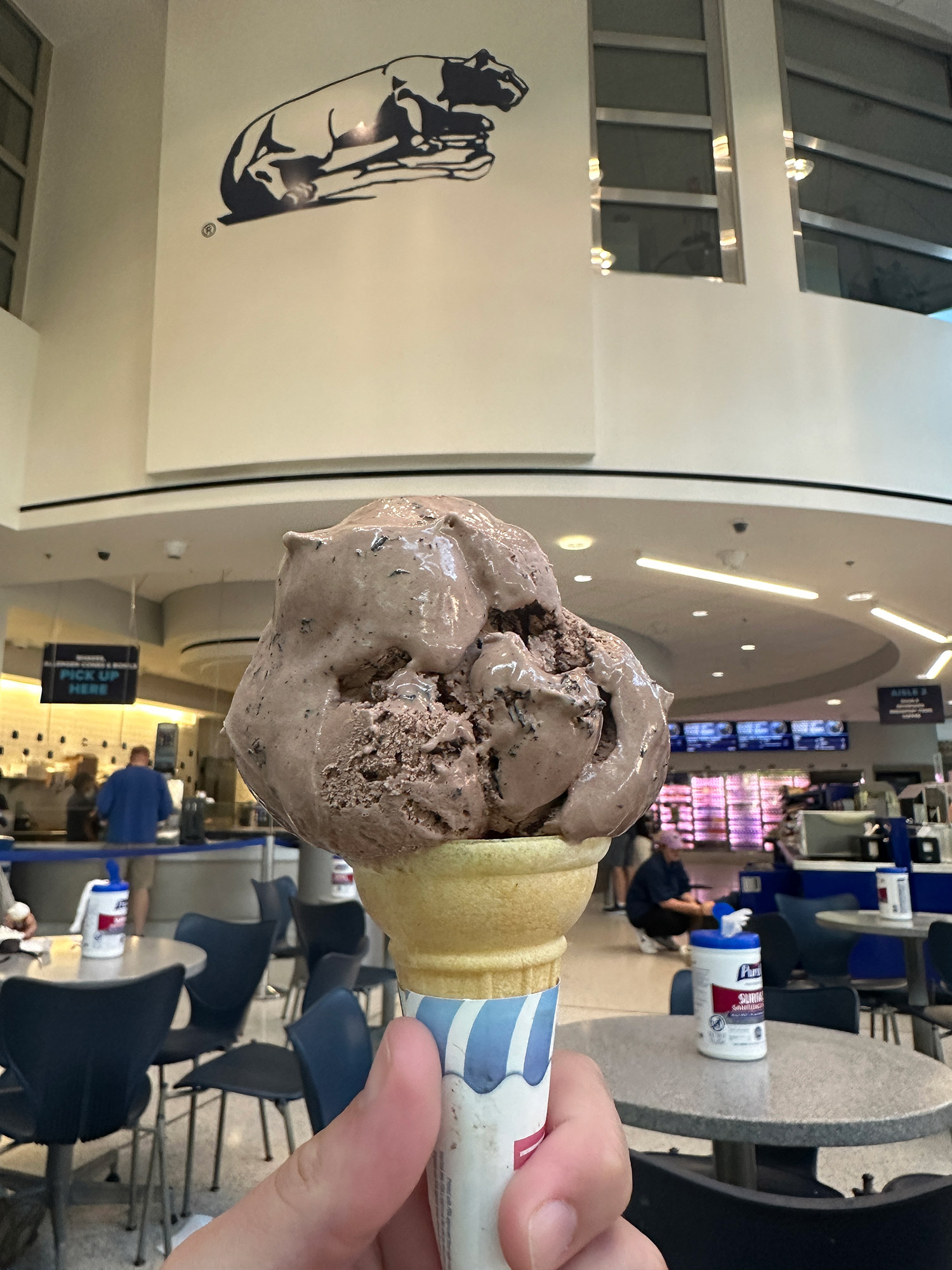 chocolate ice cream cone held in front of a Nittany Lion logo at Penn State Berkey Creamery