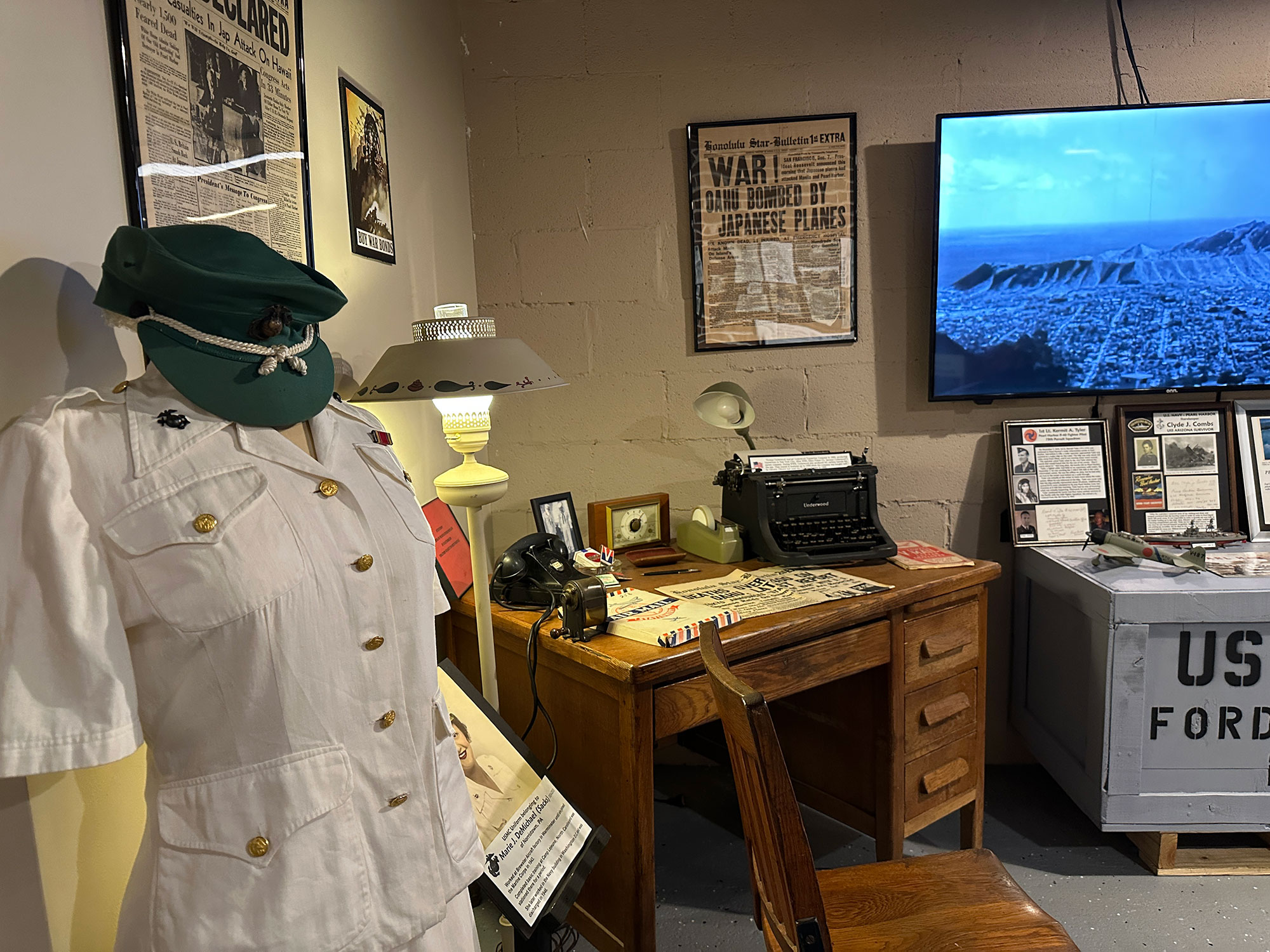 white military uniform on display next to an antique desk and a tv playing footage from World War 2