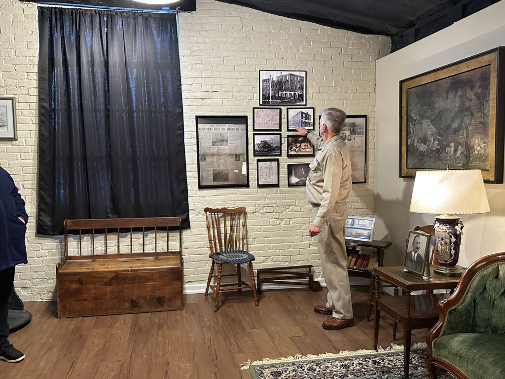 tour guide wearing a world war two era Army uniform pointing to a collage of old photos and newspaper clippings on a wall inside the Carl Spaatz Museum