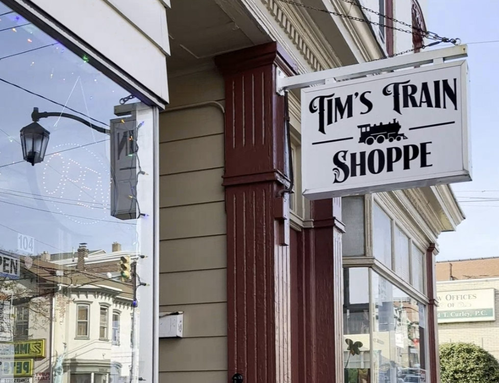 white sign with black letters reading "Tim's Train Shoppe" with an image of a train