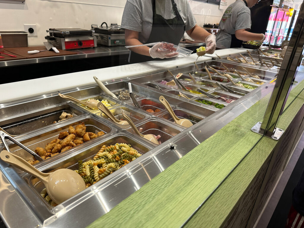Long salad bar where an employee in an apron is preparing a salad