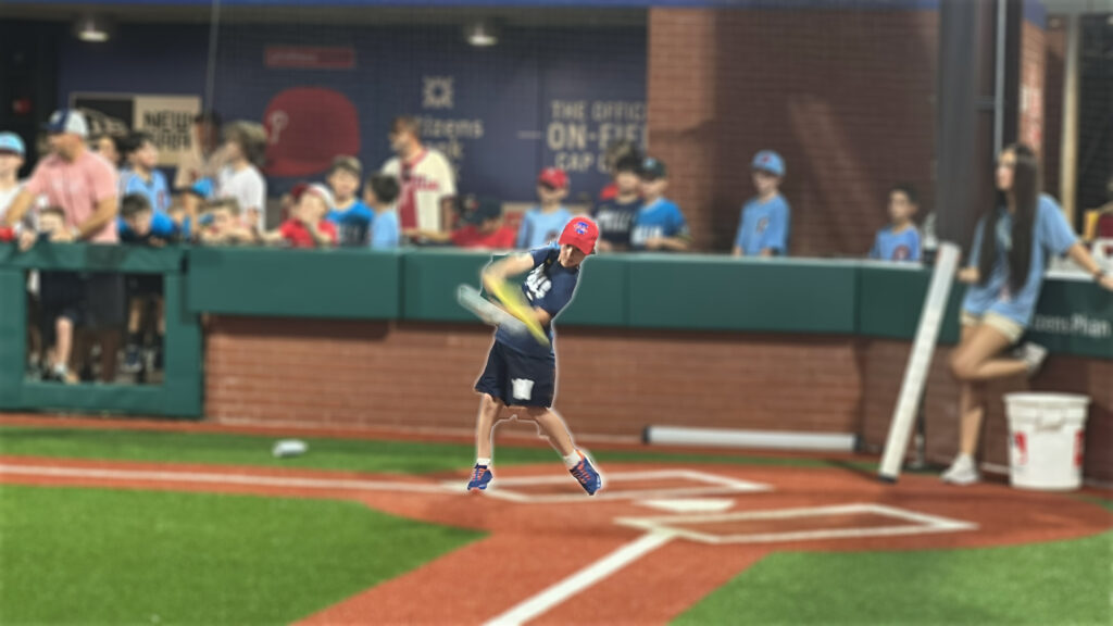 child swinging a yellow bat at a wiffle ball in a replica baseball stadium