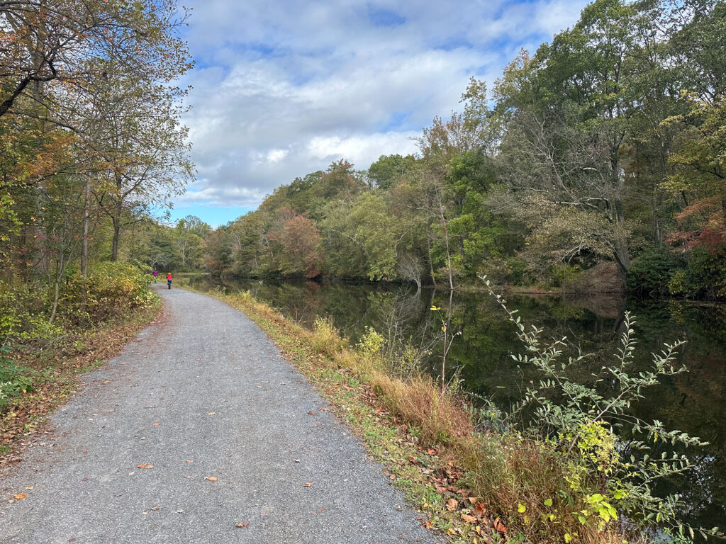 stone bicycle path with a canal on the right and green trees that are starting to turn to brown