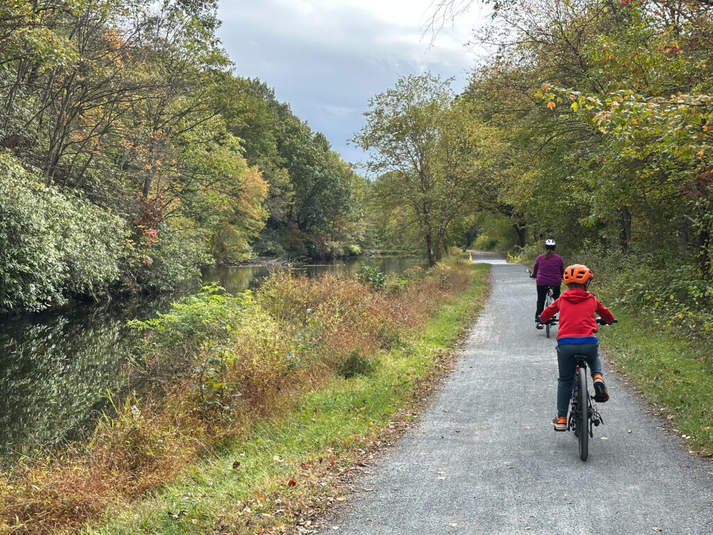 child in red sweatshirt rides a bicycle on a stone path with trees turning from green to brown